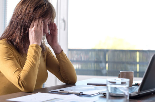 An adult woman sitting Infront of a laptop holding head in her hands due to stress.