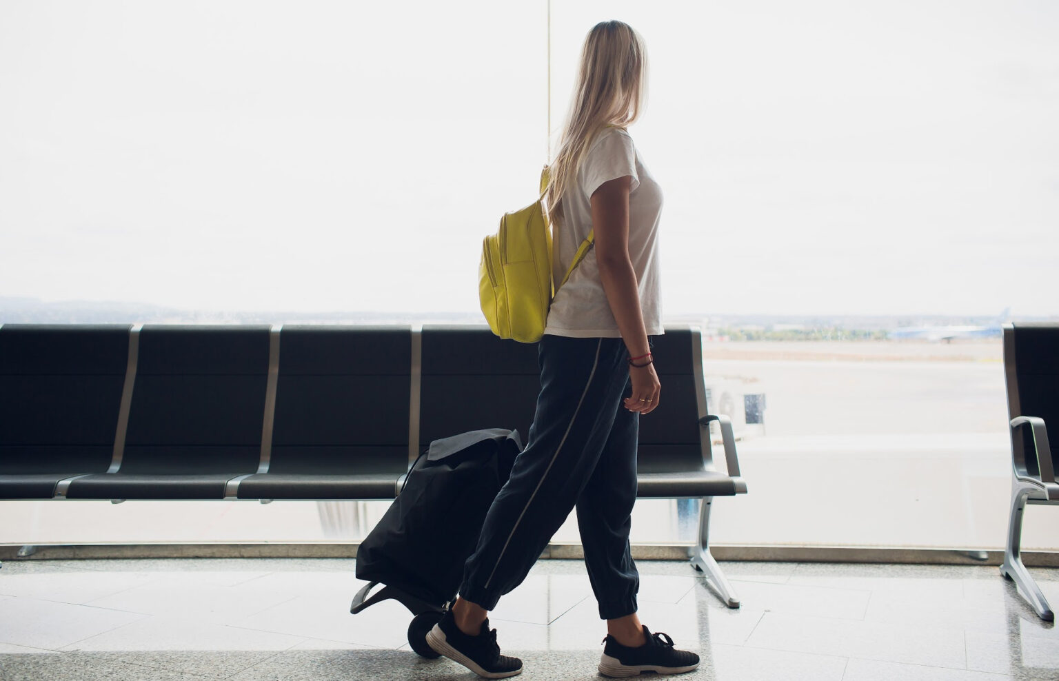 A female passenger carrying a backpack and a wheeled bag.