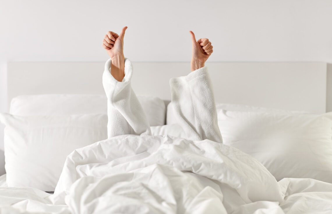 Women in a white bed giving a double thumbs up.