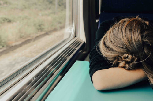 A jet-lagged woman on a train sleeping with her head on the table.