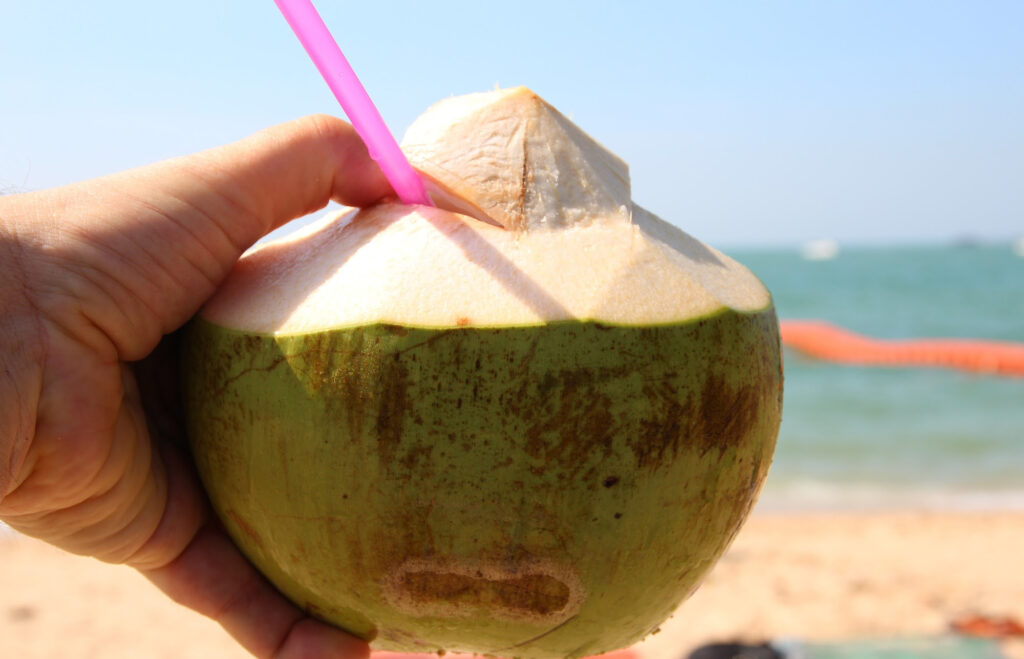 Coconut with a straw in it and a beach in the background.