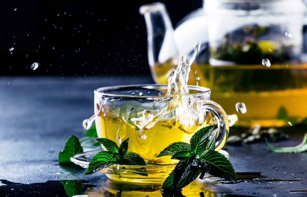 Green tea in a cup with glass teapot in the background on a black table