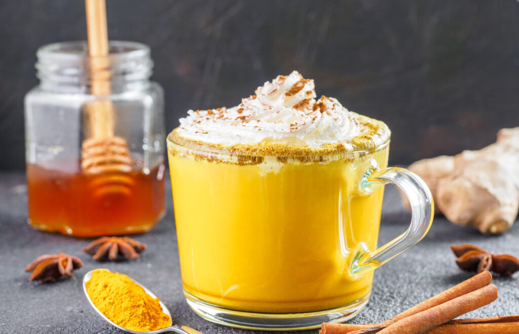 Turmeric latte in a mug on a black surface with a honey jar in the background.