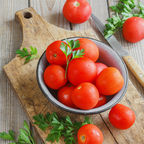 Tomatoes and cilantro in a bowl on a wooden cutting board with a wooden background