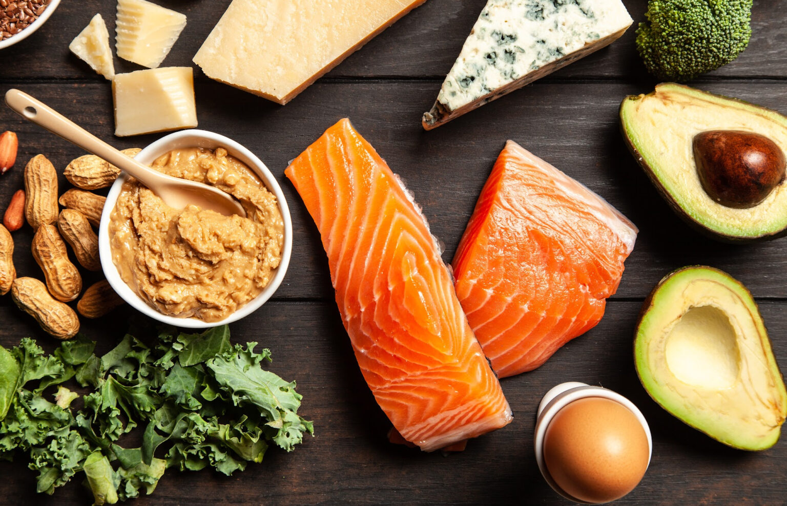 Fish, avocados, peanuts, an egg, cheese, and other healthy foods on a table.